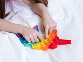 A child's hands with a popular multicolored silicone antistress toy in the shape of a unicorn on white. Fashionable Modern Touch-sensitive Children's Toy Fidget Push Push it