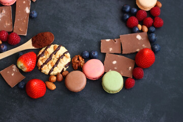 Macarons, chocolate, cookies, berries and various nuts on dark blue background. Selective focus.