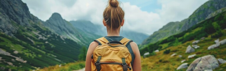 Fototapeta premium A young woman with a backpack is hiking up a mountain trail