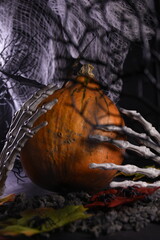Halloween. Background for the holiday. Pumpkin with leaves in the hands of a skeleton. Spiders, earth, cobweb, autumn.