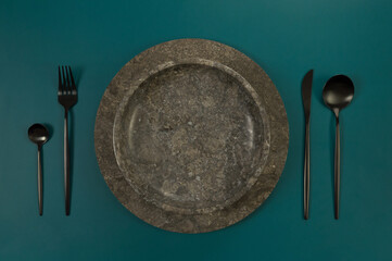 Top view of brown marble tray and plate, black cutlery on dark green background. Food presentation,...