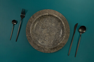 Top view of brown marble tray and plate, black cutlery on dark green background. Food presentation,...