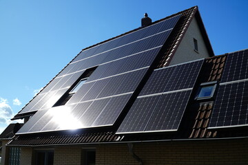 Fototapeta premium Photovoltaic installation where the glistening bright sun is reflected on the black solar panels. On an older house with a gable roof in Garbsen, Hanover district, Germany.
