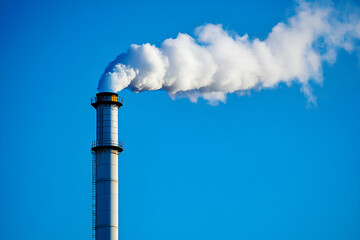 A tall industrial smokestack emitting white smoke against a clear blue sky.