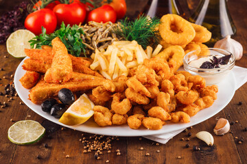 Large plate of delicious breaded seafood with french fries being served on wooden table