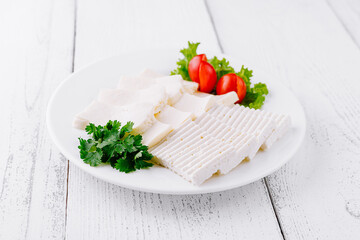 White cheese slices with cherry tomatoes and parsley on white plate