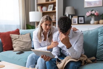 Young businesswoman comforting her husband at home while he reading negative statistics of his business company trade on digital tablet. Togetherness and emotional support.