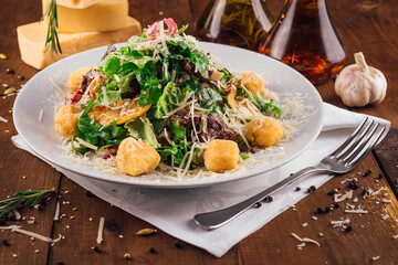 Fresh salad with meat and croutons being served on a wooden table