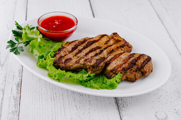 Grilled steak lying on fresh lettuce with tomato sauce on white plate