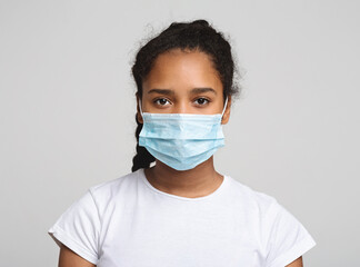 Flu concept. Teen african girl with protective face mask, grey studio background