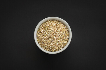 Raw Quinoa seeds in a white bowl on a black background