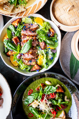 A vibrant food arrangement featuring a salad with grilled meat and citrus slices, alongside a green soup garnished with herbs. Perfect for culinary presentations and food photography.