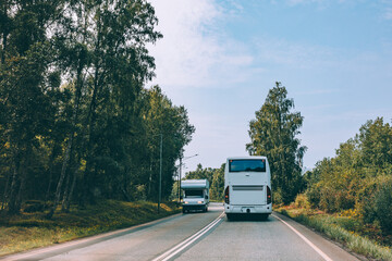 White bus and Caravan trailer or Camper rv driving on asphalt road between fall or summer woods in the rural landscape in Finland.