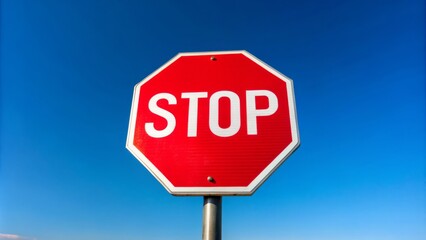 Obraz premium **STOP** in bold white letters on a red octagonal sign suspended from a metal pole against a brilliant