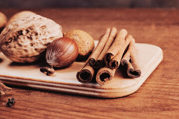 fragrant cinnamon sticks, walnuts, nutmeg and clove buds lie on a wooden board close-up, top view