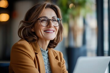 Happy mature middle aged professional business woman bank worker or hr manager, corporate executive looking away at work working on laptop computer in office thinking of business technology future