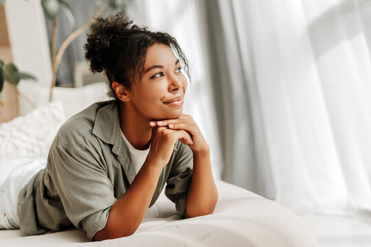 Young woman lying on bed is daydreaming looking up away from camera