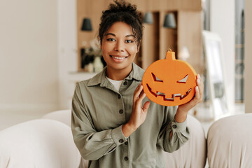 Woman holding a jack o'lantern decoration smiling at home