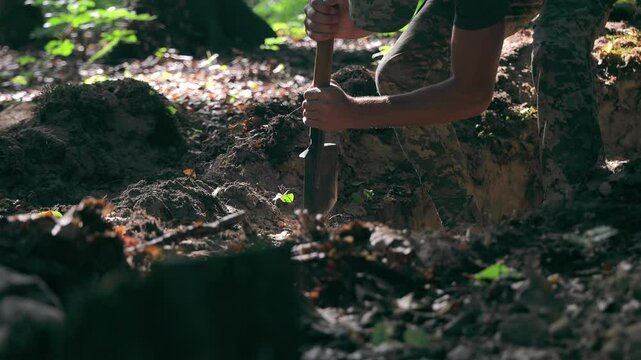 A Ukrainian soldier digs trenches in the forest during military operations. A soldier digs in the forest with a shovel, prepares a defensive position or a trench.