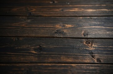 Fototapeta premium A close-up view of a dark table made of wood planks arranged horizontally. The surface of the table is aged and textured, with natural wood grain patterns. Grunge wooden background.