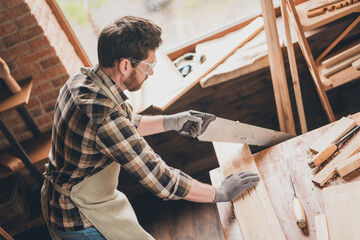 Photo of focused guy artisan working with wood plank cut saw in garage