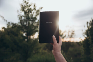 Man holds the Bible in a sunlit outdoor setting