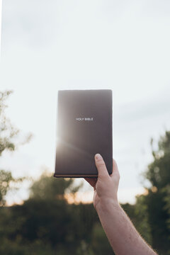 Hand holding a Bible against a soft sunset backdrop