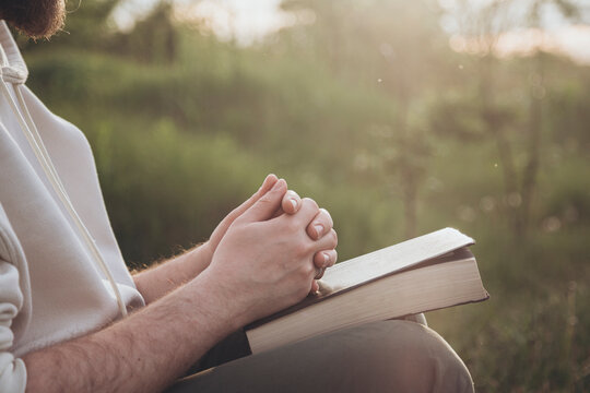 Man praying while holding a Bible sitting outdoors