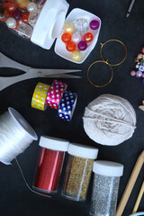 Colorful beads, coloring pencils, glitter, needles, string, hoop, tape and scissors on dark...