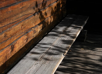 a rustic wooden bench in the shadow of an old wooden cabin wall
