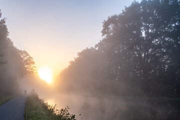 Naklejka premium A peaceful and tranquil sunrise is beautifully illuminating a misty river that is surrounded by lush trees