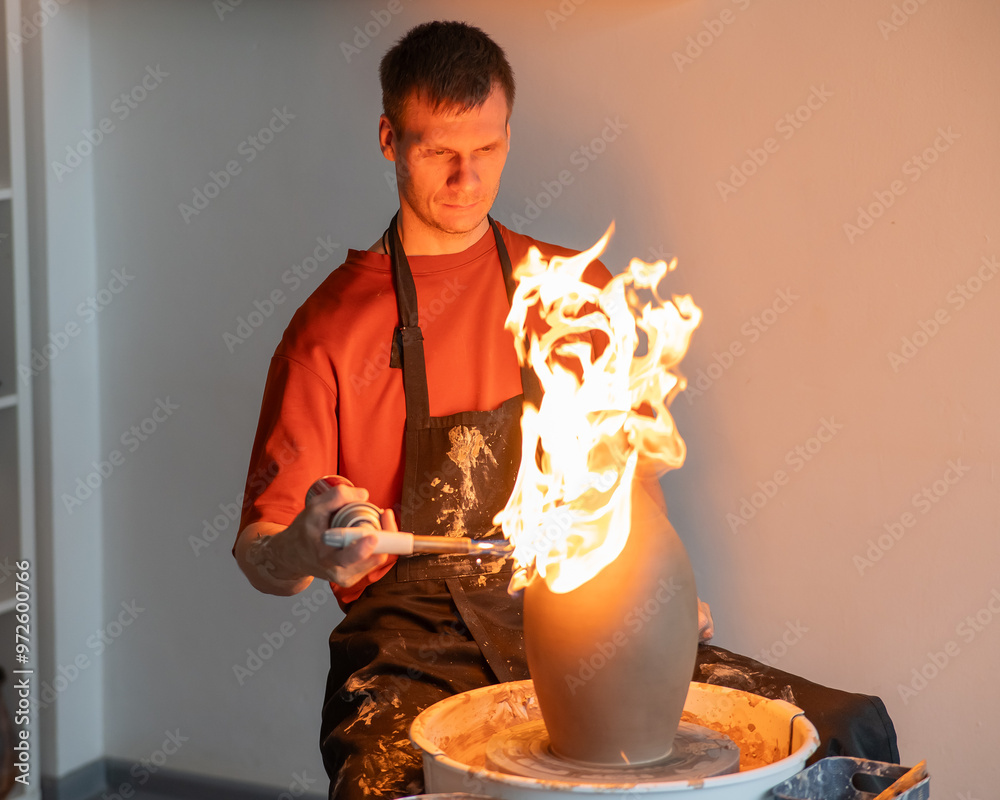 Wall mural a potter burns a jug with a gas burner on a potter's wheel.