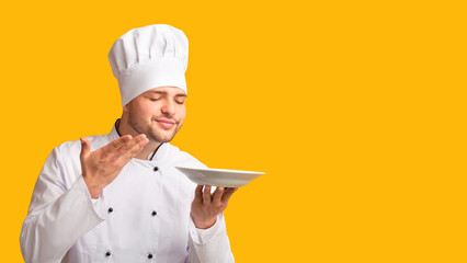 Professional Male Chef Holding Empty Plate Smelling The Aroma Of Invisible Dish Over Yellow Studio...
