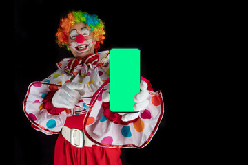 Funny clown with smartphone with green screen for template, man entertainer as Joker in a suit and...