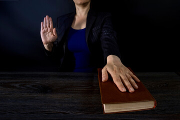 Female hand on the Bible and on the constitution book during the inauguration in parliament or the oath in court. Woman taking Oath of Office. Dark background, blue office clothes.