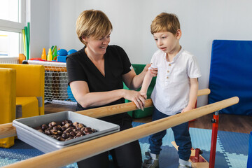 Physical therapist assists a young cute boy with cerebral palsy during rehabilitation exercises on...