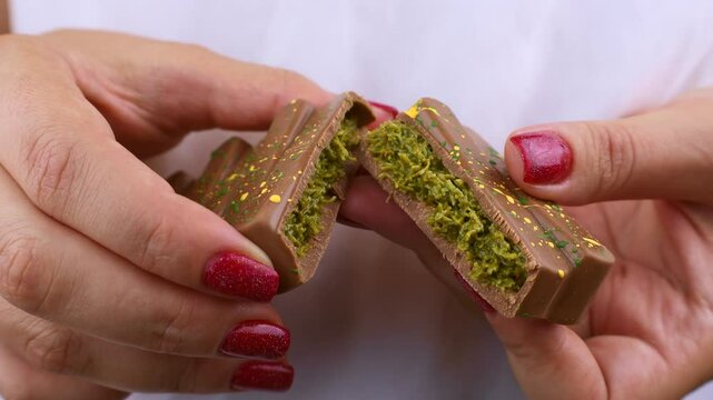 Female hands breaking off Dubai Chocolate bar with green kadayif and pistachio spread with pistachio nuts close up