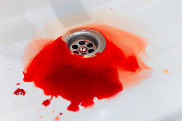 A pool of real blood running down a bathroom sink drain. Concept of human blood loss