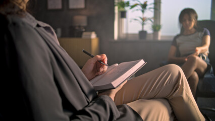 Psychological office: Female therapist takes notes in notebook, listens to teenager. Upset African American teenage girl discusses problems, finds solution during therapy session with psychologist. © Framestock