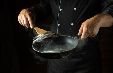 Frying capelin in a hot frying pan. The chef puts the small fish into the frying pan with a kitchen spatula. Fish diet concept for a restaurant or hotel