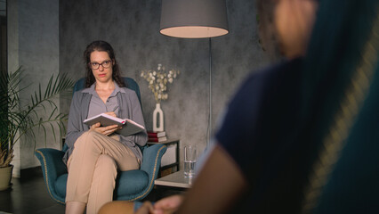 Female psychologist takes notes in notebook, listens to patient, communicates and asks questions....