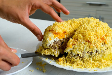 Woman cooking cuts mimosa salad with knife on kitchen at home, hands close-up. Preparing dish at home. Cuisine, culinary, recipe. Traditional Russian food to eat on holidays, weekend.