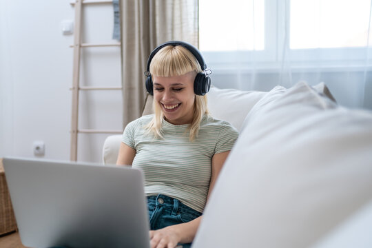 Young happy freelance worker or university student woman sitting work at home on sofa working on laptop, while listening podcast or listen the music, favorite song, enjoying freedom and independence.