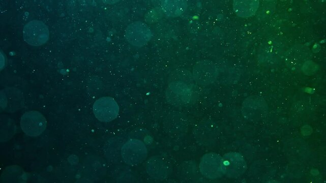 Abstract water background with dark blue and green glow. Chaotically moving glowing dust particles in water. Color mixing in water. Glare underwater. Macro world. Textured. Space effect
