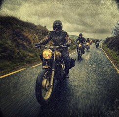 A group of bikers riding motorcycles on a country road, led by an older man in a leather jacket and helmet.