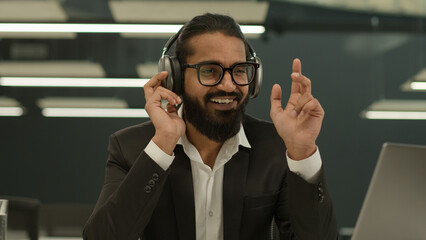 Indian businessman relaxed Arabian man business worker office entrepreneur enjoying listening to music in wireless modern headphones earphones laptop listen audio song at workplace work musical pause