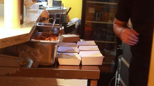 Video of a unrecognizable person placing hamburger buns into takeout boxes during meal preparation in a busy restaurant kitchen, 4K resolution