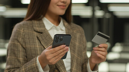 Asian woman business lady Korean girl Chinese client Japanese customer Malaysian businesswoman indoors in office holding mobile phone credit bank plastic card buy shopping online payment banking order