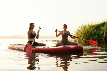 Sport conception. Women friends are on sup board on the lake together