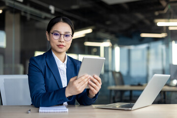 Asian businesswoman using tablet in office environment. Professional attire, confident expression....